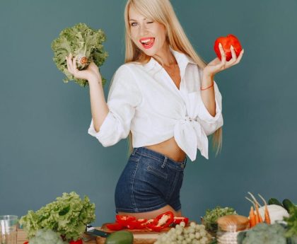 Cheerful woman in white shirt holding lettuce and pepper, celebrating fresh vegetables.